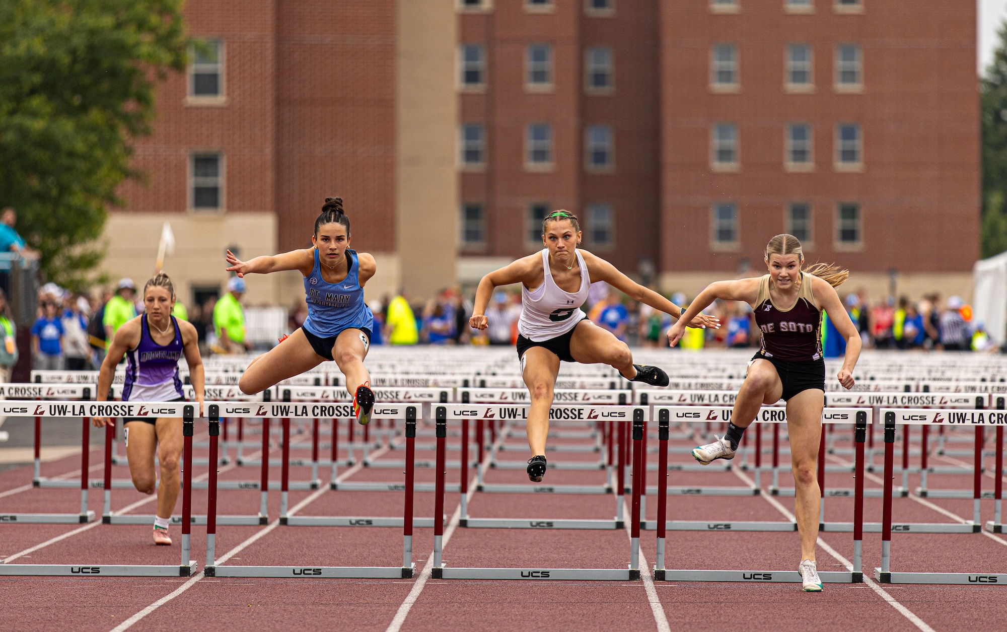 High school girls compete in a hurdles race during a WIAA track and field championship meet
