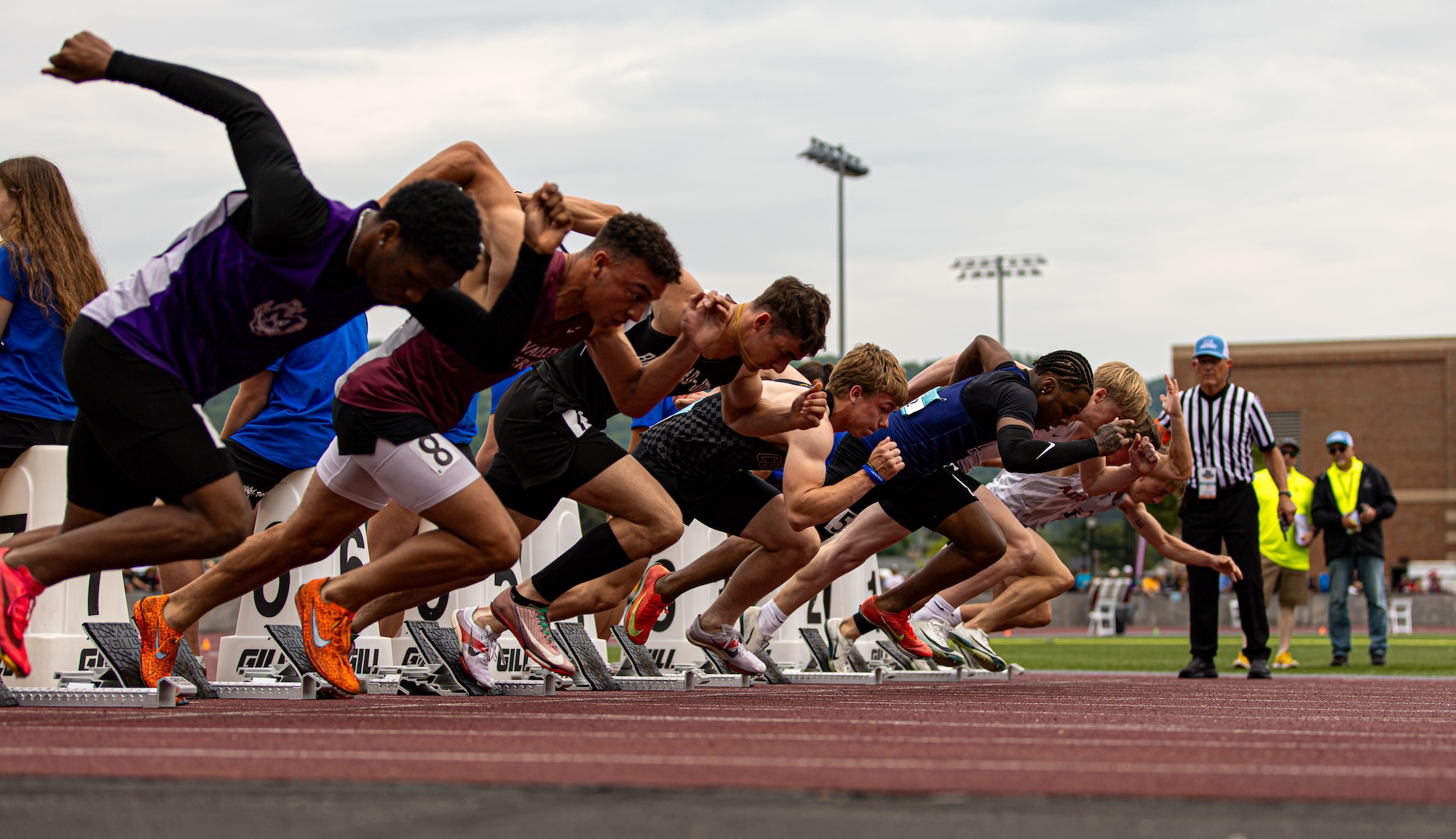 A group of male students lined up side-by-side on a track preparing to begin their race.