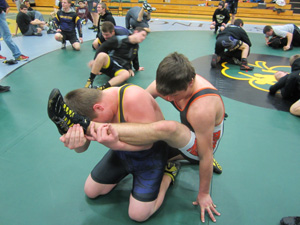 Two wrestlers practice a defensive position on the mat, with one wrestler holding the other’s raised leg during a drill.