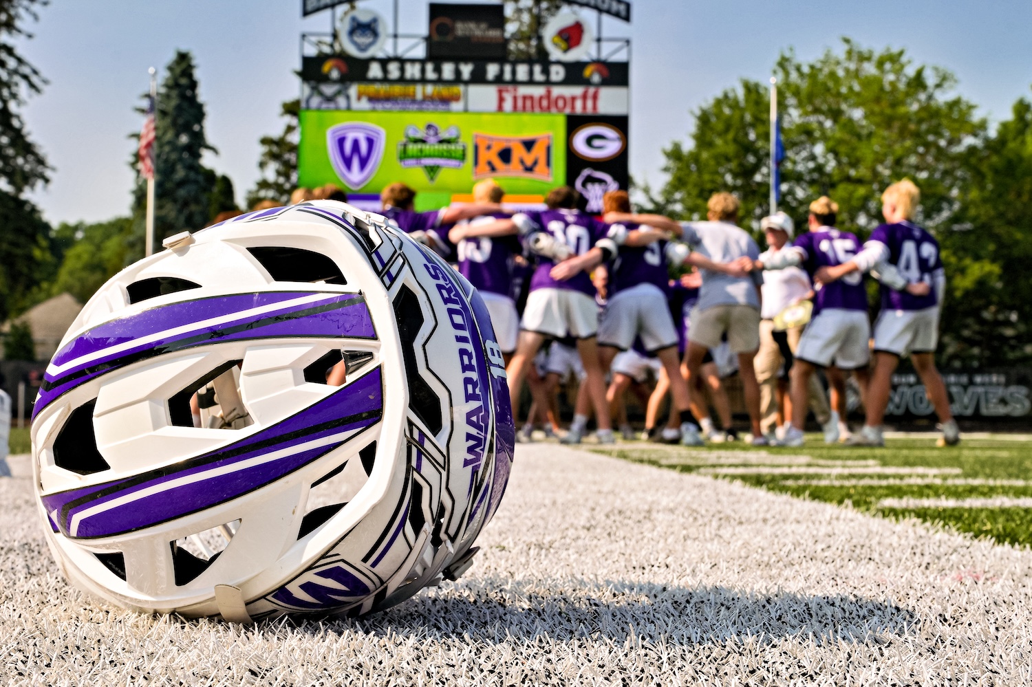 Lacrosse Helmet in Frame with Team celebrating behind.