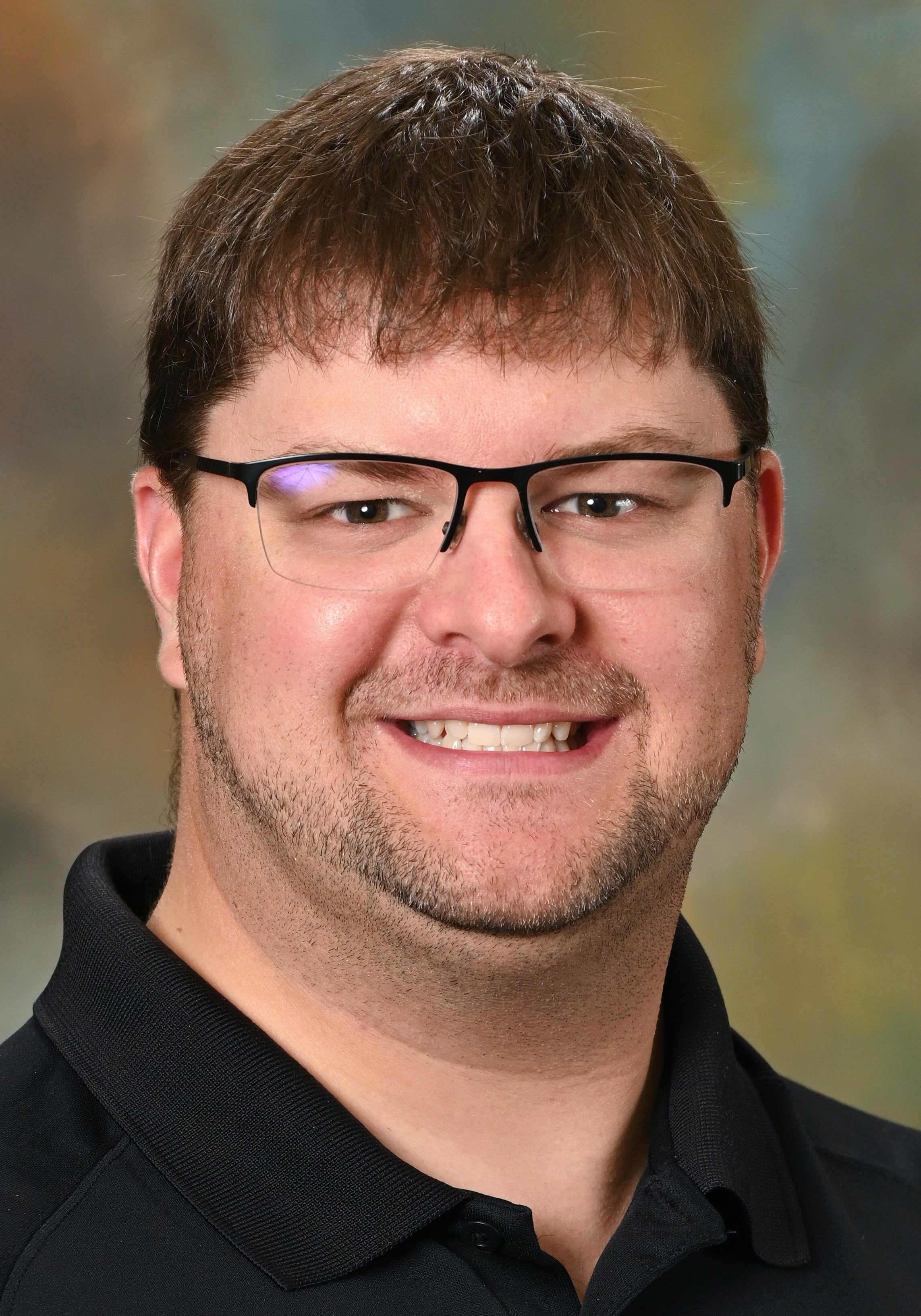 Smiling man wearing glasses and a black polo shirt posing for a professional headshot.