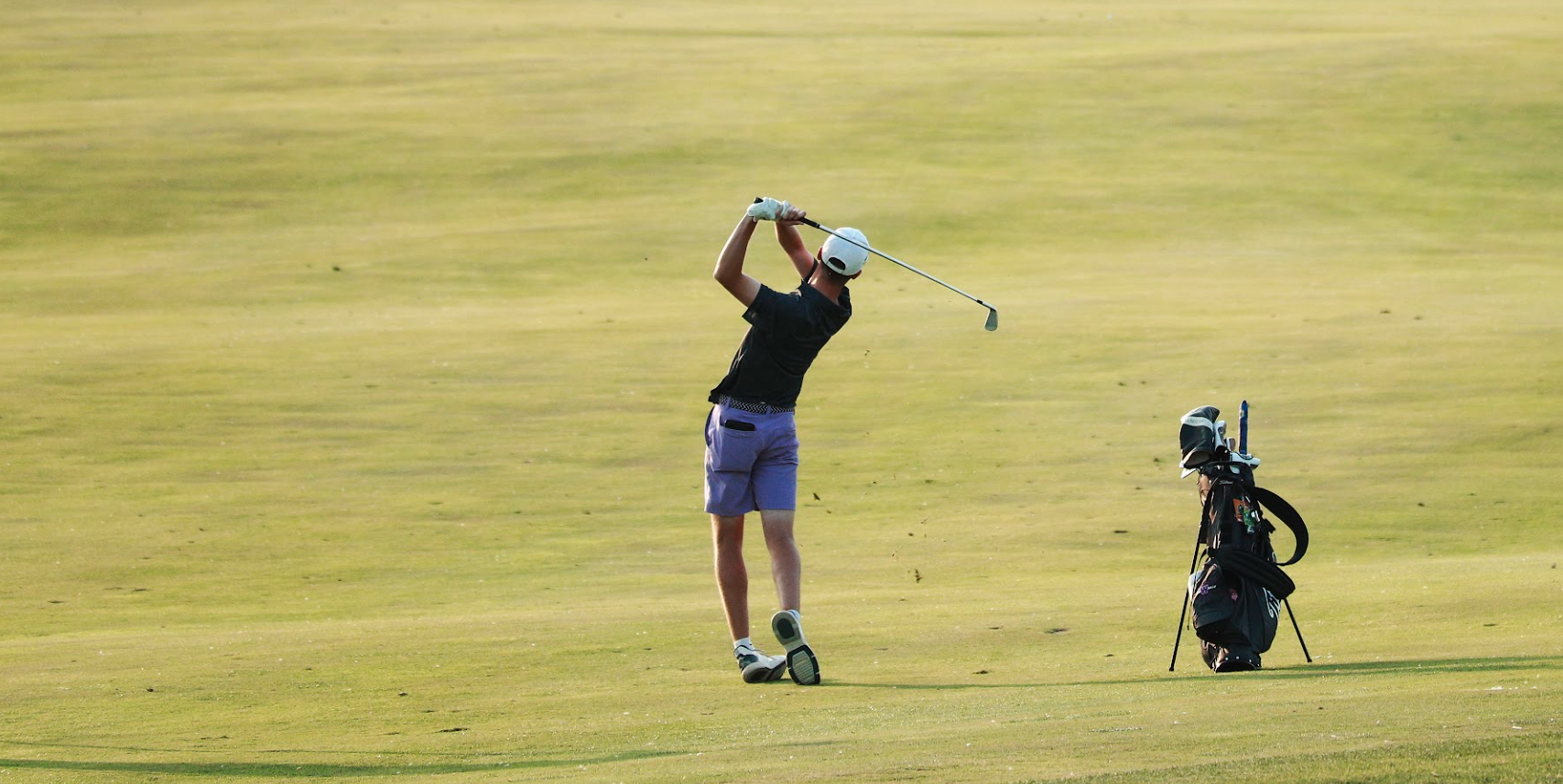a boy is seen faraway on a field playing golf after hitting a ball 