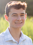 Smiling young man in a light plaid shirt standing outdoors.