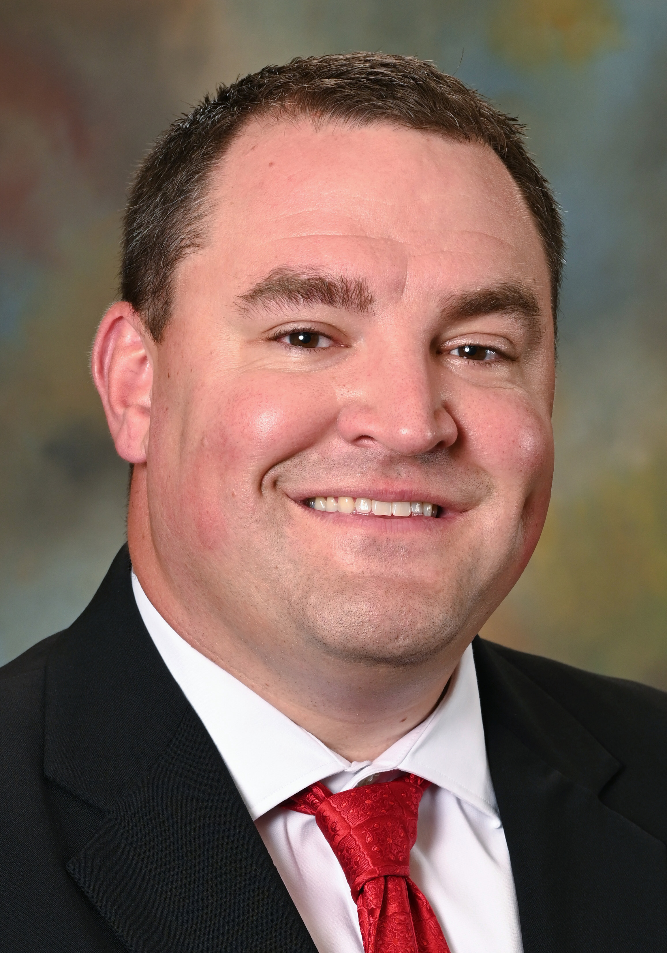 Smiling man in a suit and red tie posing for a professional headshot.
