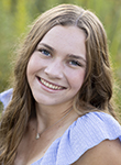 A smiling young woman poses outdoors for a portrait with greenery in the background.