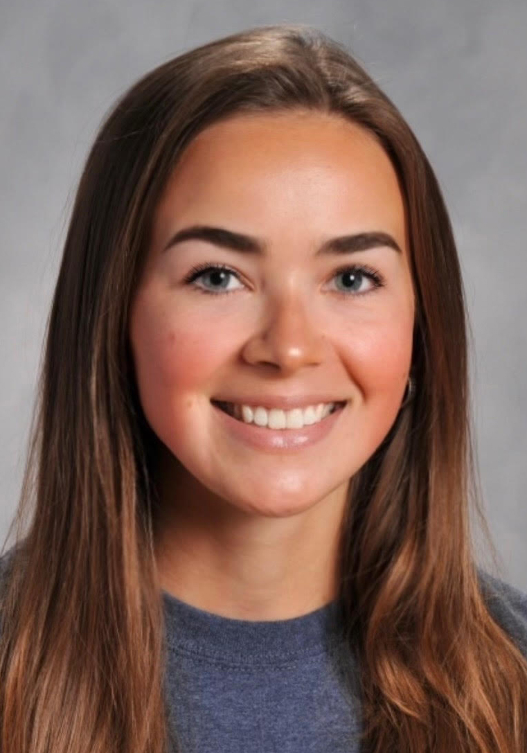 Headshot of a smiling woman with long brown hair wearing a gray top against a gray background.