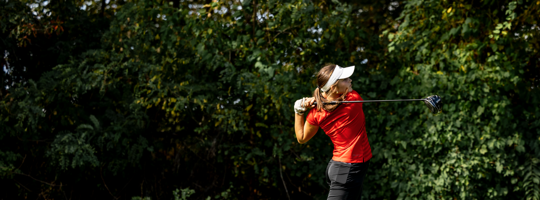 a woman is seen playing golf against a lush green background