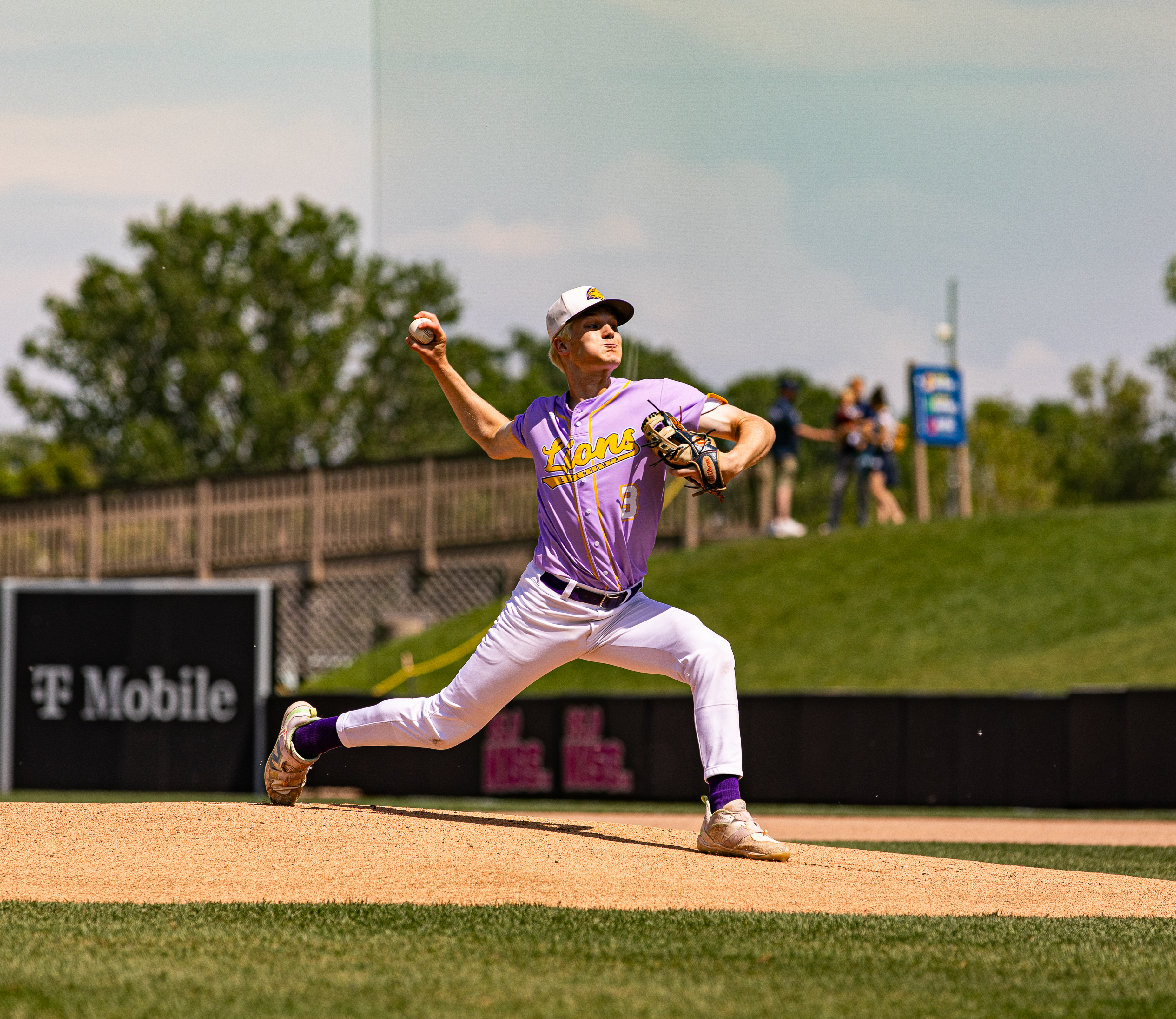 Baseball pitcher in a purple Lions uniform throws from the mound during a game.