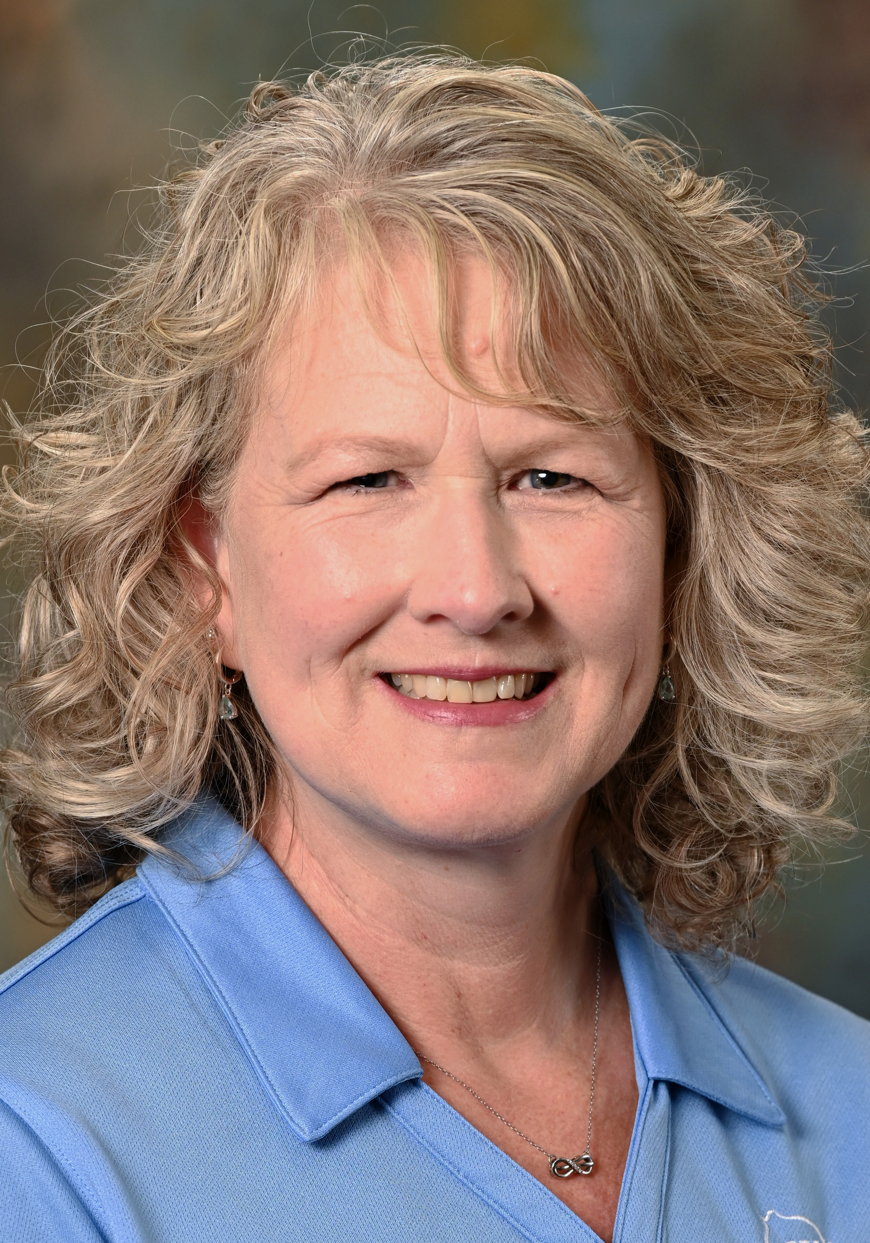 Headshot of a smiling woman with curly blonde hair wearing a light blue collared shirt.