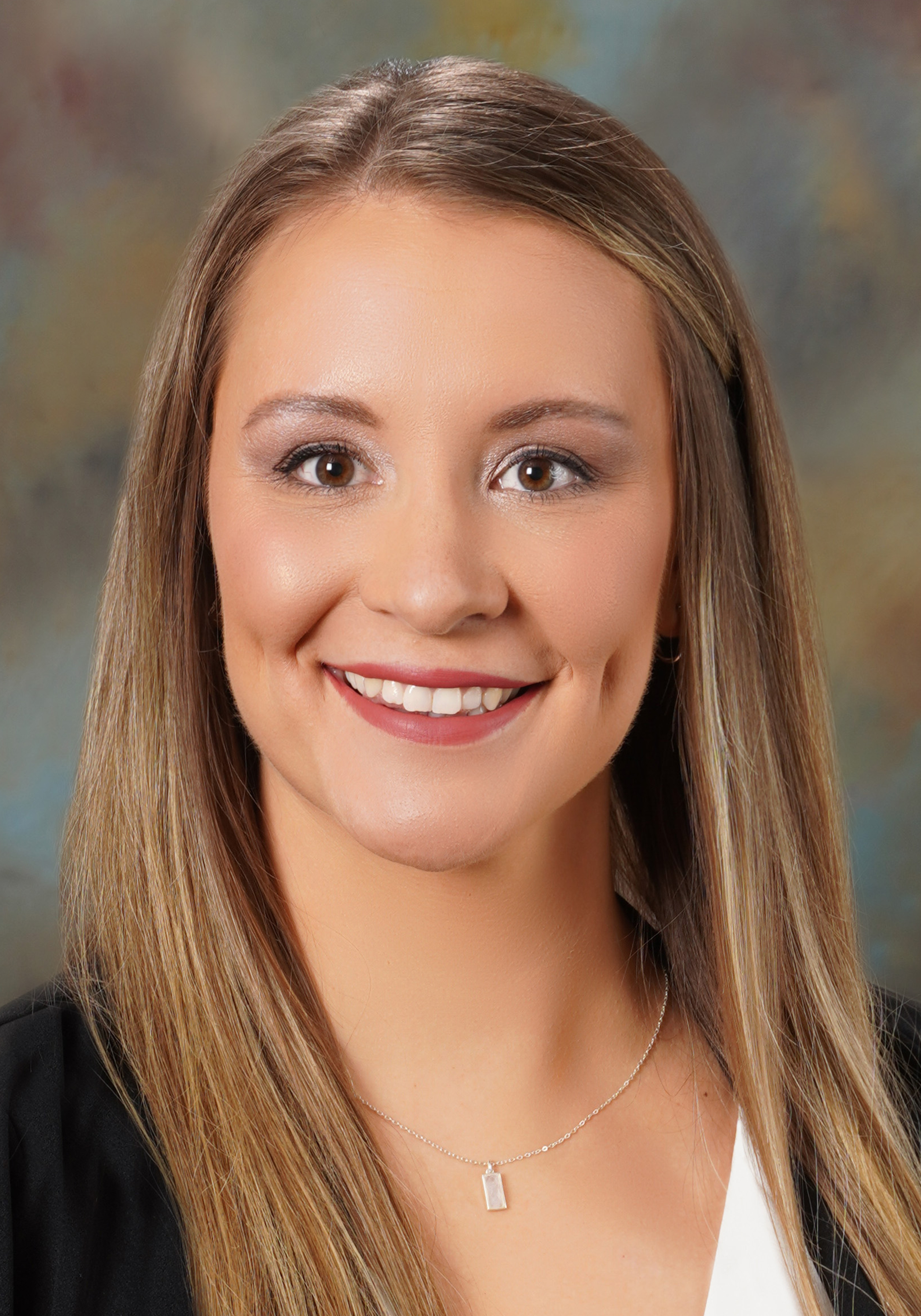 Headshot of a smiling woman with long highlighted hair wearing a black blazer, white top, and necklace.