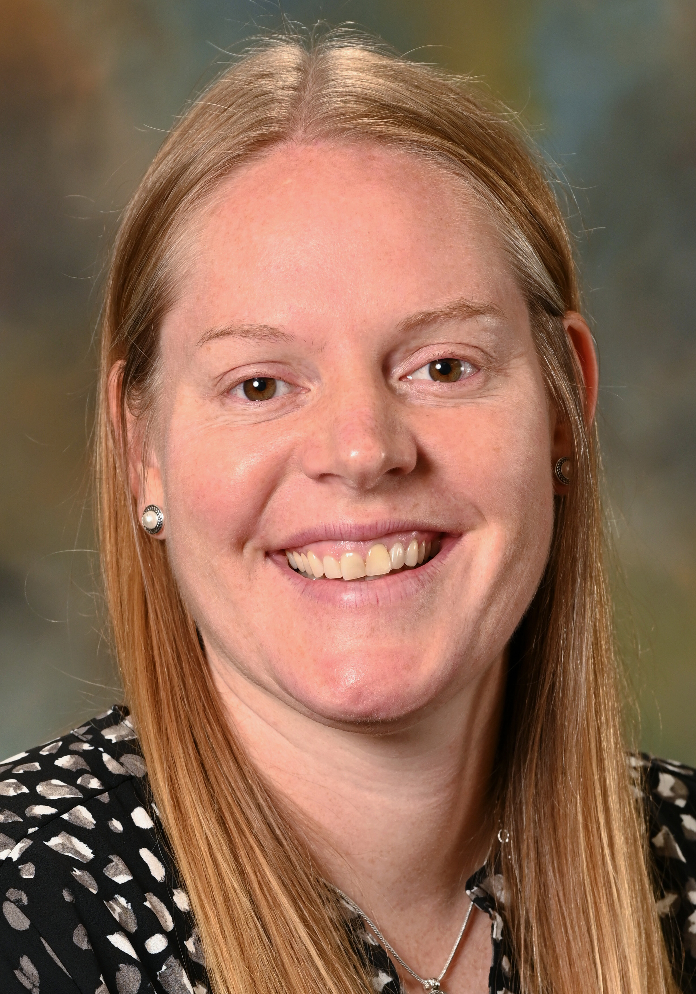 Headshot of a smiling woman with long straight blonde hair wearing a black patterned top.