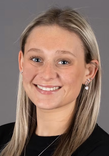Headshot of a smiling woman with straight blonde hair wearing a black top against a gray background.