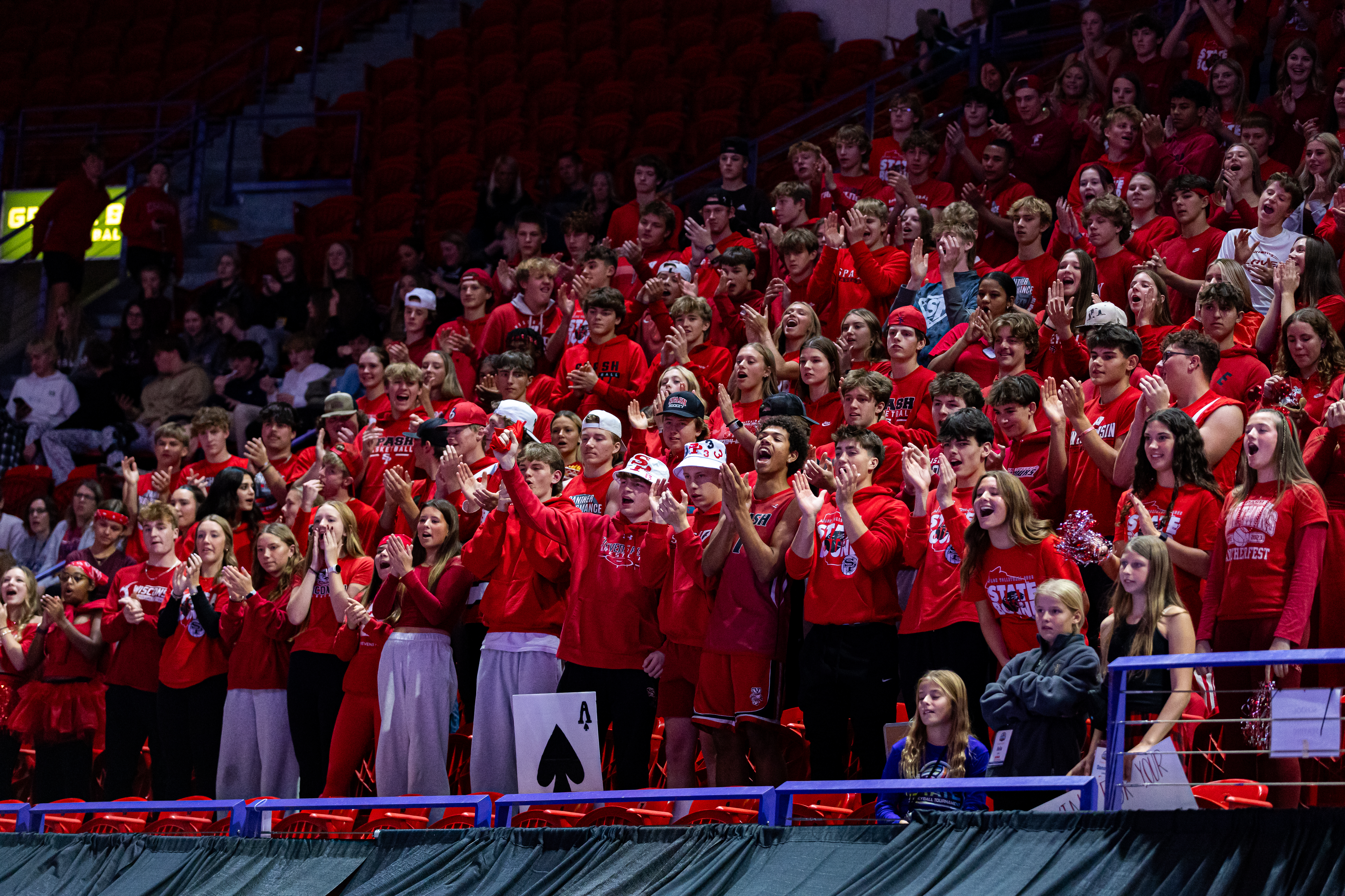 A large crowd of students dressed in red cheers from the stands during a sporting event.