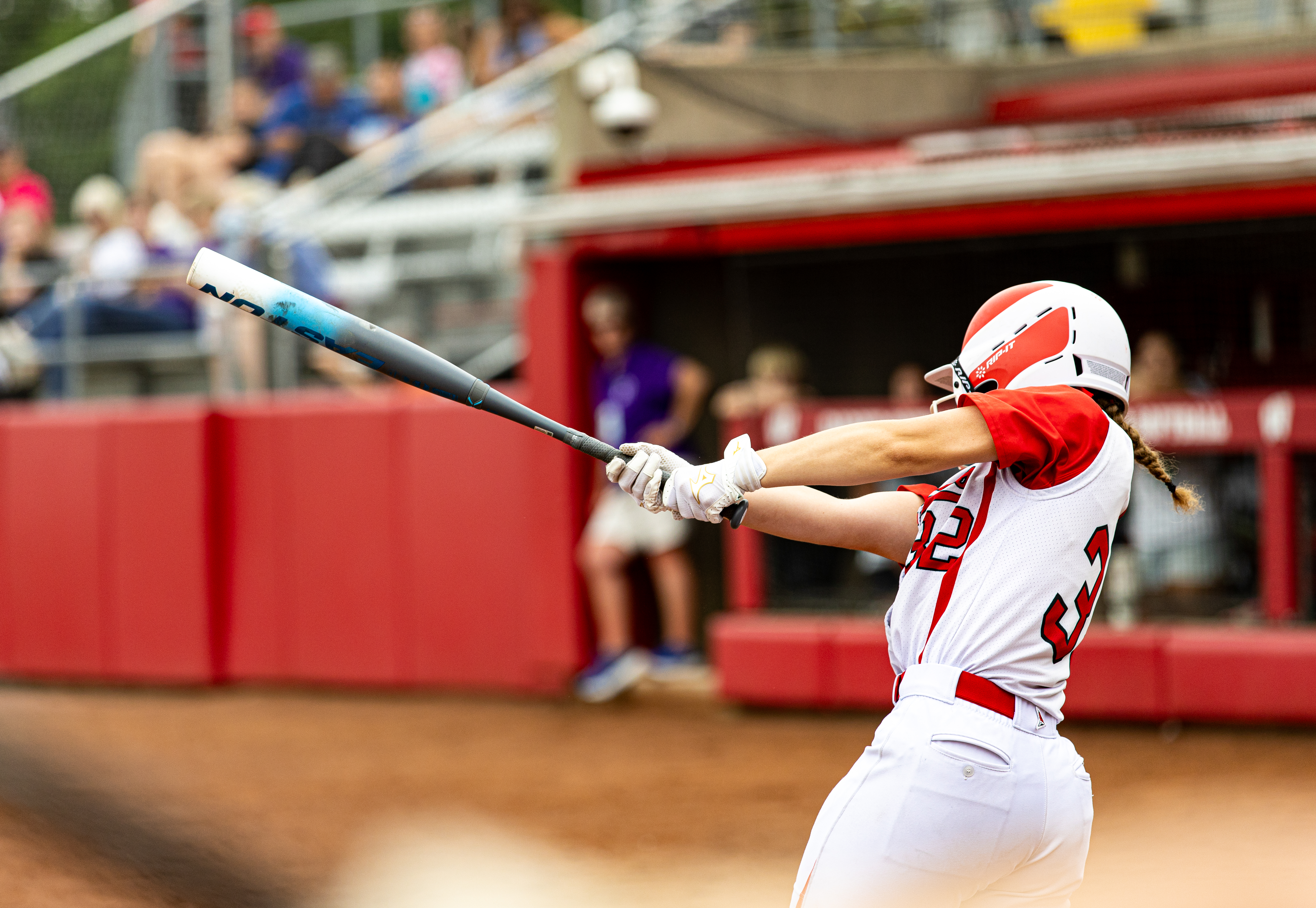 A softball player in a white and red uniform swings a bat during a game.