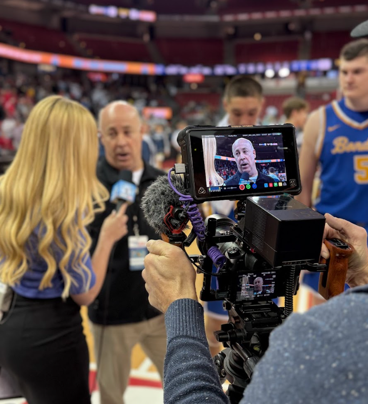 an interview with a coach is seen through a camera operators camera