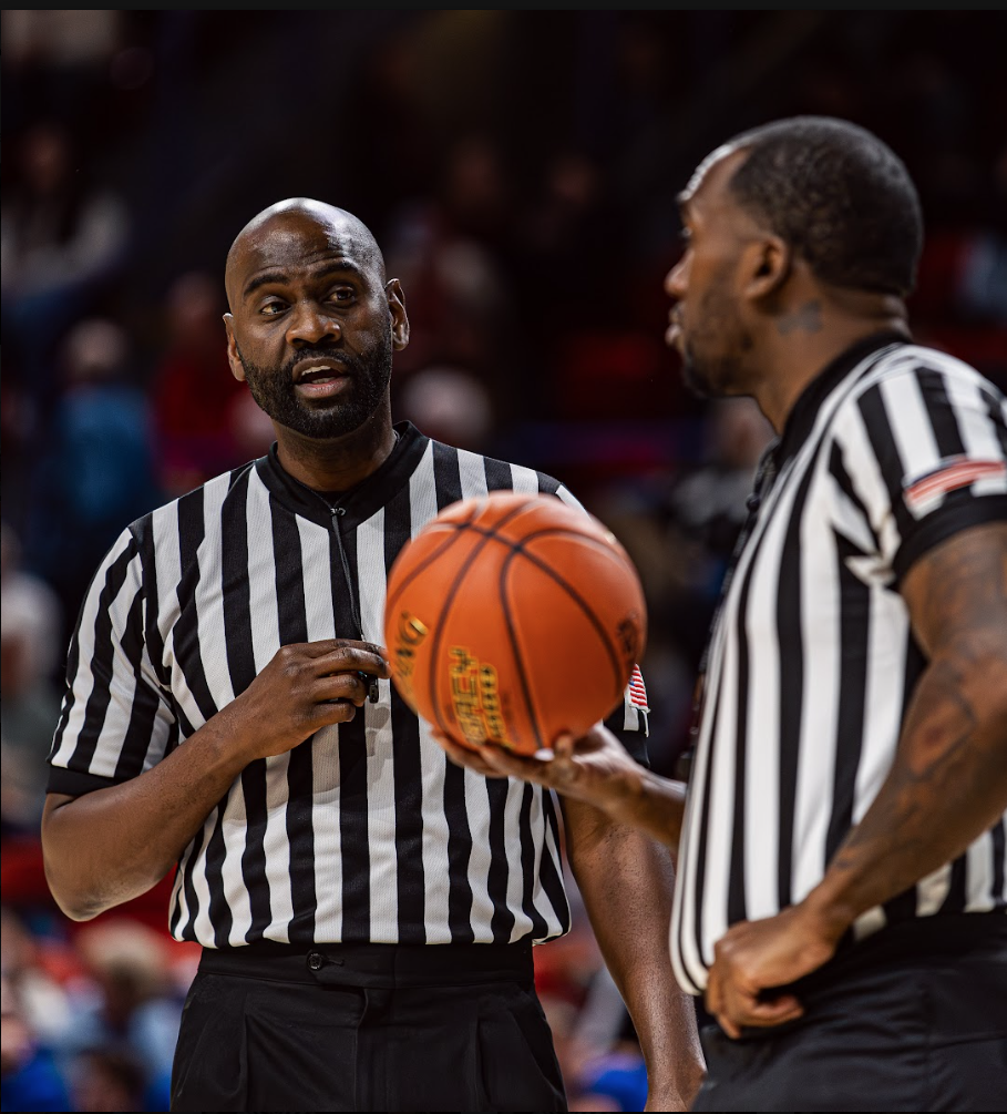 two basketball officials are talking while one holds a basketball