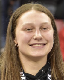 Young woman with long light brown hair smiling in an indoor gym setting.
