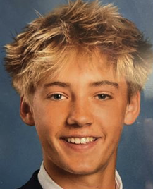 Young man with tousled blond hair smiling in a formal portrait photo.
