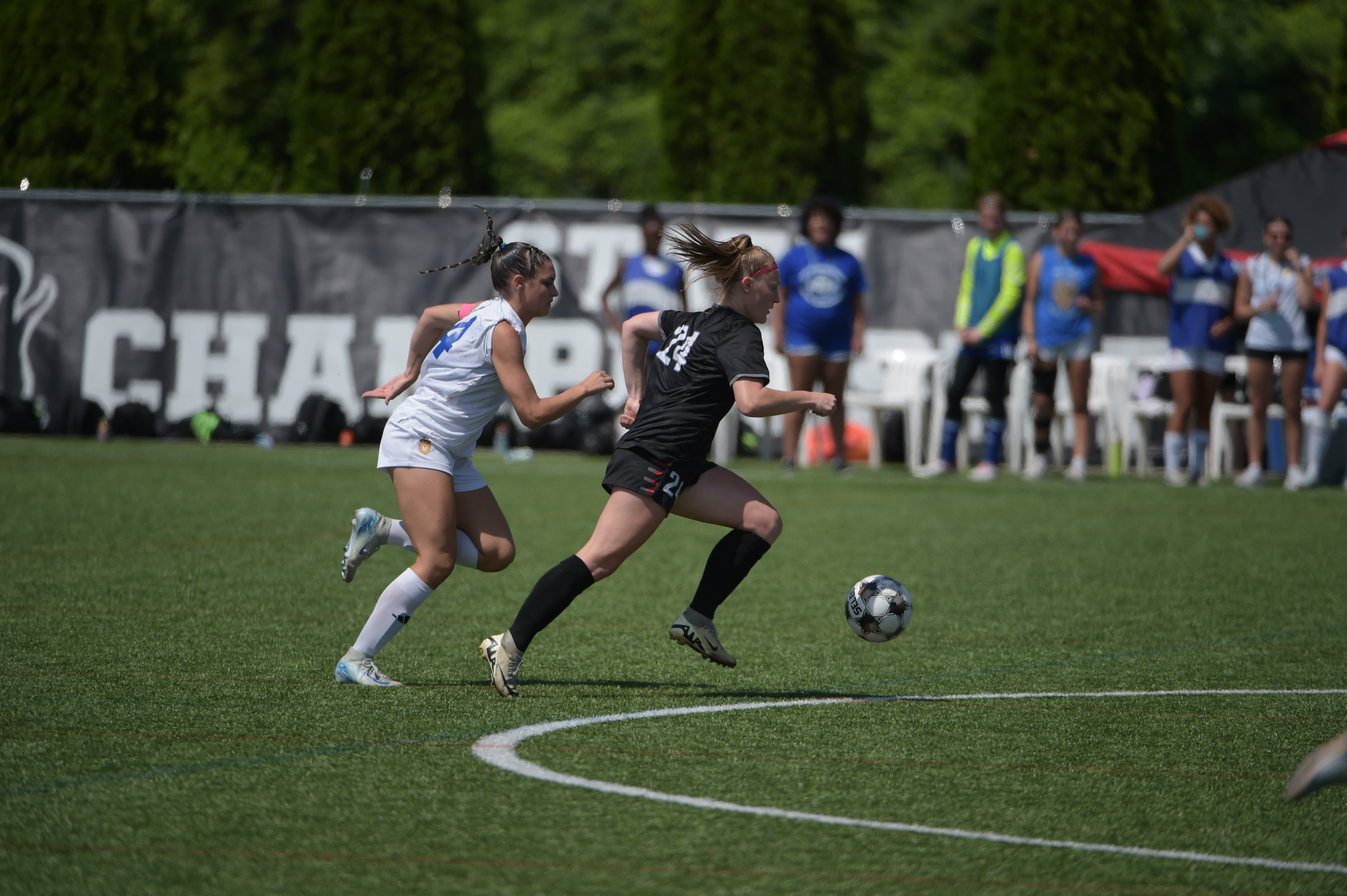 Two soccer players chase the ball during a game on an outdoor field.