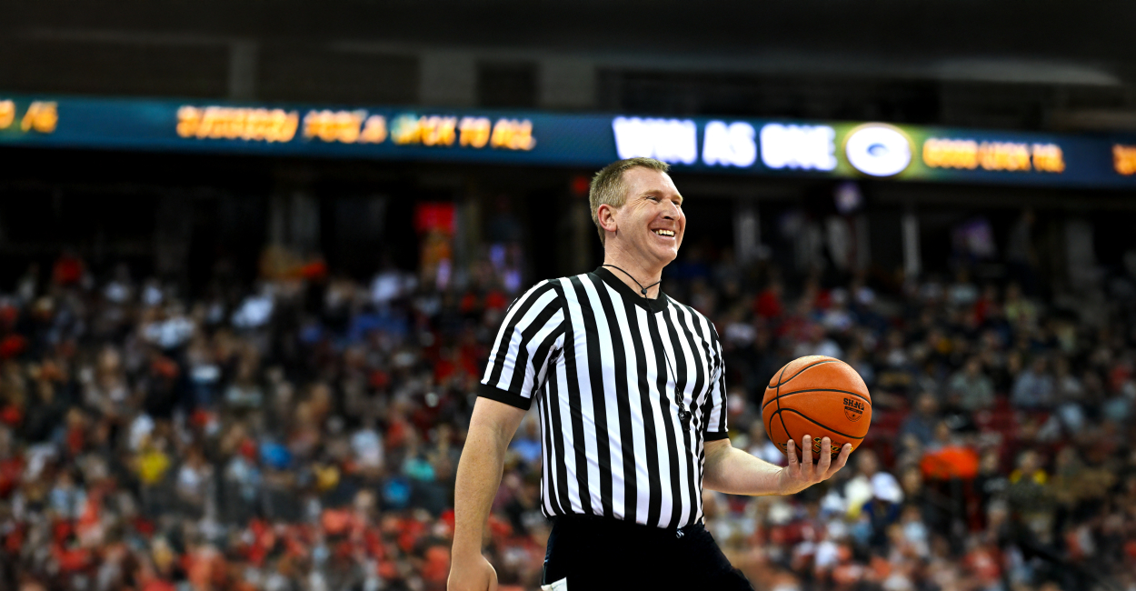 Photo of male basketball referee, holding ball at the state tournament with a crowd behind him