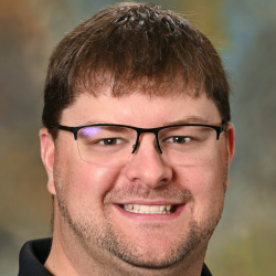 Smiling man wearing glasses and a black polo shirt posing for a professional headshot.