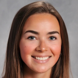 Headshot of a smiling woman with long brown hair wearing a gray top against a gray background.