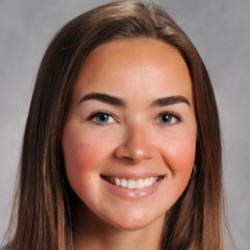 Headshot of a smiling woman with long brown hair wearing a gray top against a gray background.