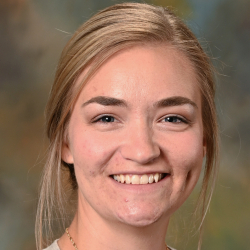 Headshot of a smiling woman with blonde hair pulled back, wearing a light gray cardigan and gold necklace.
