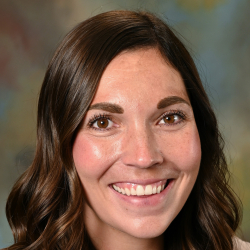 Headshot of a smiling woman with long wavy brown hair wearing a light blazer and white top.