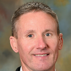 Man in a suit and red plaid tie posing for a professional headshot.