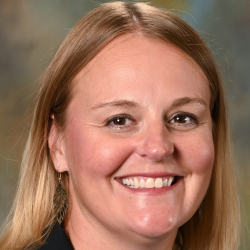 Headshot of a smiling woman with shoulder-length blonde hair wearing a black blazer and white top.
