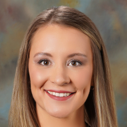 Headshot of a smiling woman with long highlighted hair wearing a black blazer, white top, and necklace.