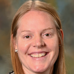 Headshot of a smiling woman with long straight red hair wearing a black patterned top.