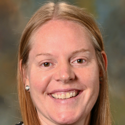 Headshot of a smiling woman with long straight blonde hair wearing a black patterned top.