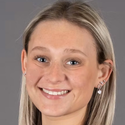 Headshot of a smiling woman with straight blonde hair wearing a black top against a gray background.