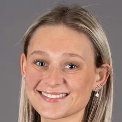 Headshot of a smiling woman with straight blonde hair wearing a black top against a gray background.